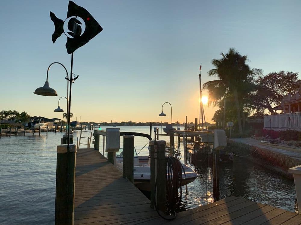 Sunset over a waterfront dock with a fish sign and palm trees in the background.