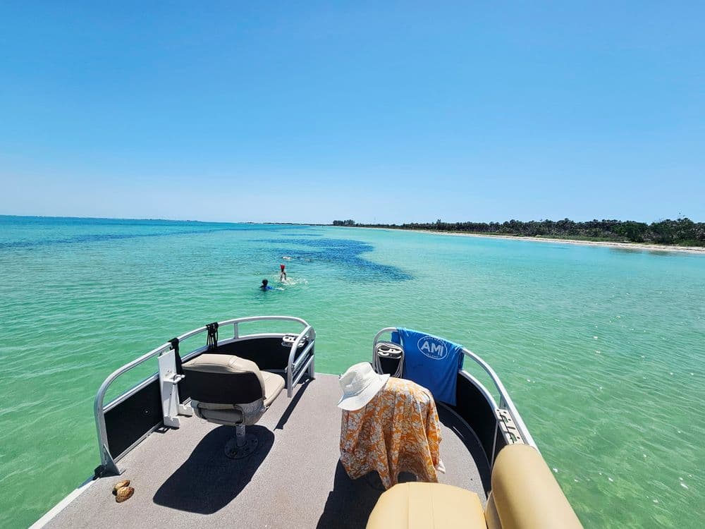 View from a boat on clear water with people swimming and a beach in the background.