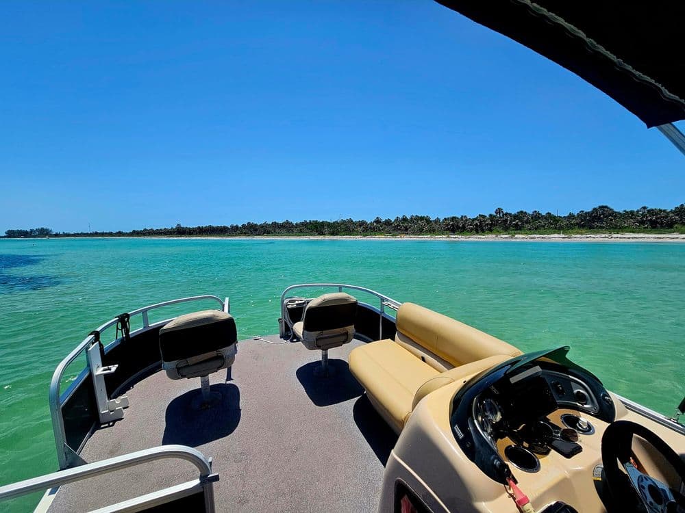 Pontoon boat navigating clear turquoise waters with a scenic shoreline view.